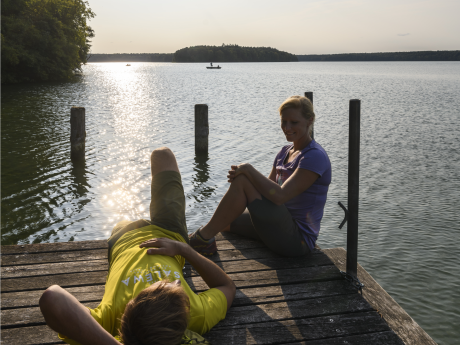 Bild von zwei Personen auf einem Bootssteg am See in der Abendsonne