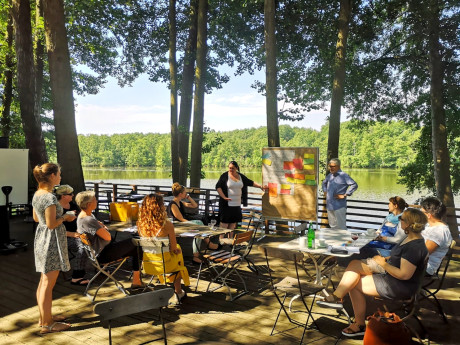 Menschengruppe, die auf einer Terrasse am See sitzt und einen Workshop durchführt.