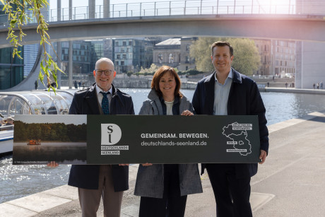 Kooperationspartner Deutschlands Seenland stehen am Wasser und halten ein Plakat