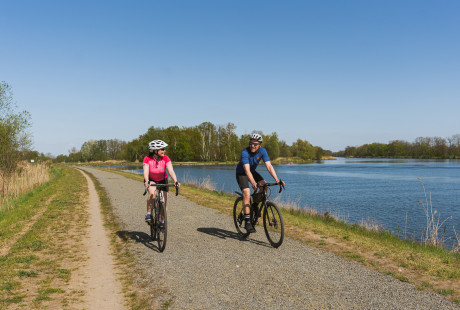 Paar auf Gravelbikes fahren auf Radweg neben einem Gewässer in Brandenburg