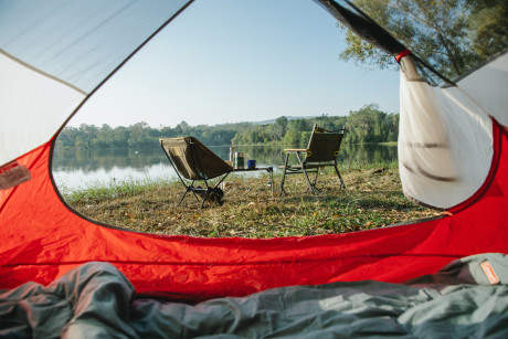 Blick aus einem Zelt auf Campingtisch mit Stühlen und See im Hintergrund