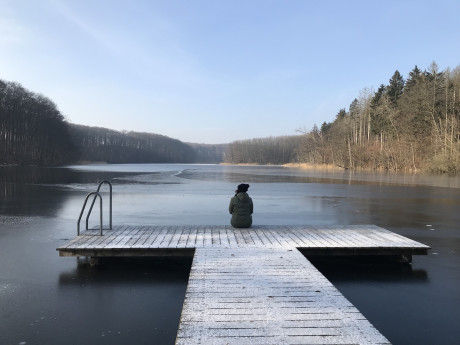 Person sitzt auf dem Steg eines winterlichen Sees in der Uckermark