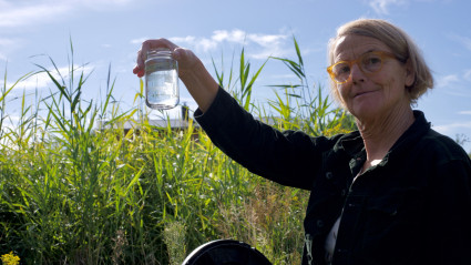 Frau hält ein Glas mit einer Wasserprobe aus dem Pflanzenklärbeet des Rehof Rutenberg