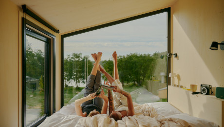 Zwei Personen lesen gemeinsam ein Buch auf dem Bett einer kleinen Lodge am See