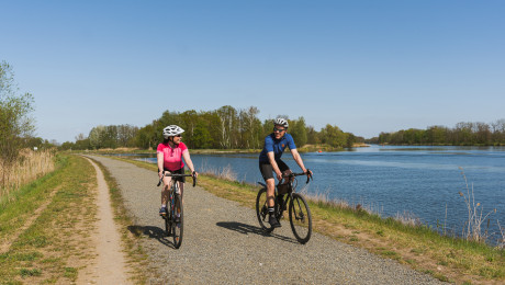 Paar auf Gravelbikes fahren auf Radweg neben einem Gewässer in Brandenburg
