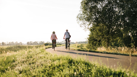 Ein weiblicher und ein männlicher Radfahrer auf einem Radweg zwischen Feldern im Sommer unterwegs