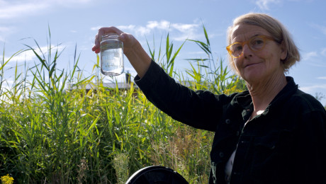Frau hält ein Glas mit einer Wasserprobe aus dem Pflanzenklärbeet des Rehof Rutenberg