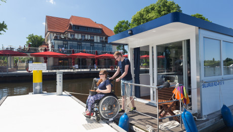 Eine Rollstuhlfahrerin legt vom Hausboot ab. Der Steg ist barrierefrei.