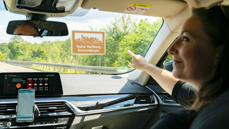 Zwei Personen im Auto passieren ein touristisches Hinweisschild an der Autobahn